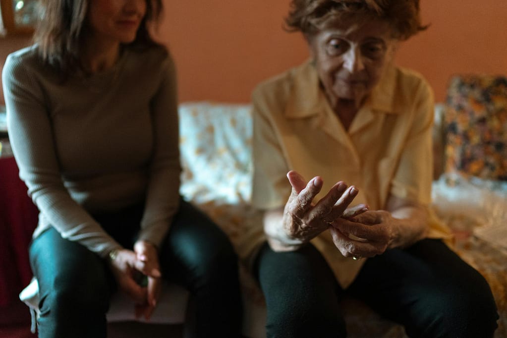 An elderly woman and her caregiver share a moment on the couch, embodying companionship.