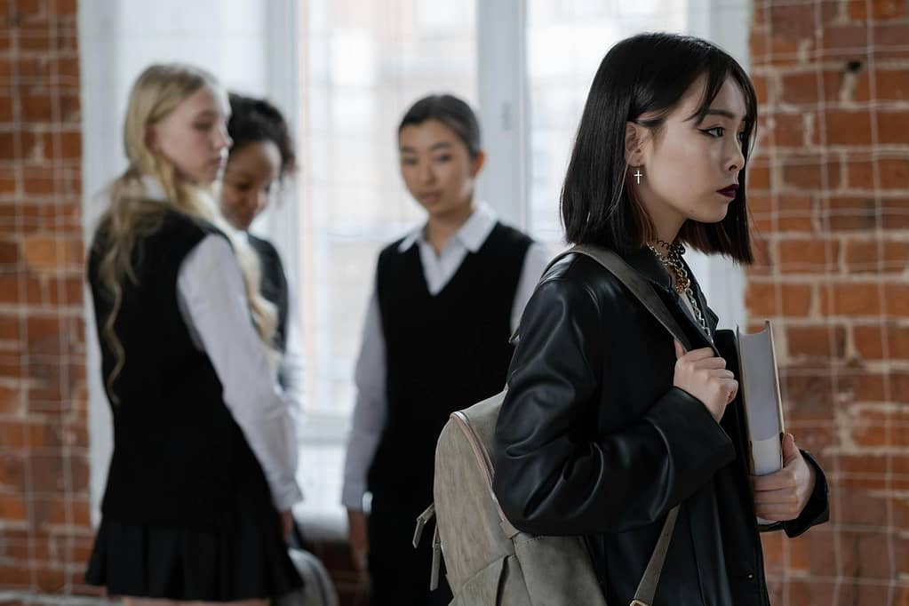 A teenage girl walks away from a group of classmates, reflecting themes of isolation and bullying.