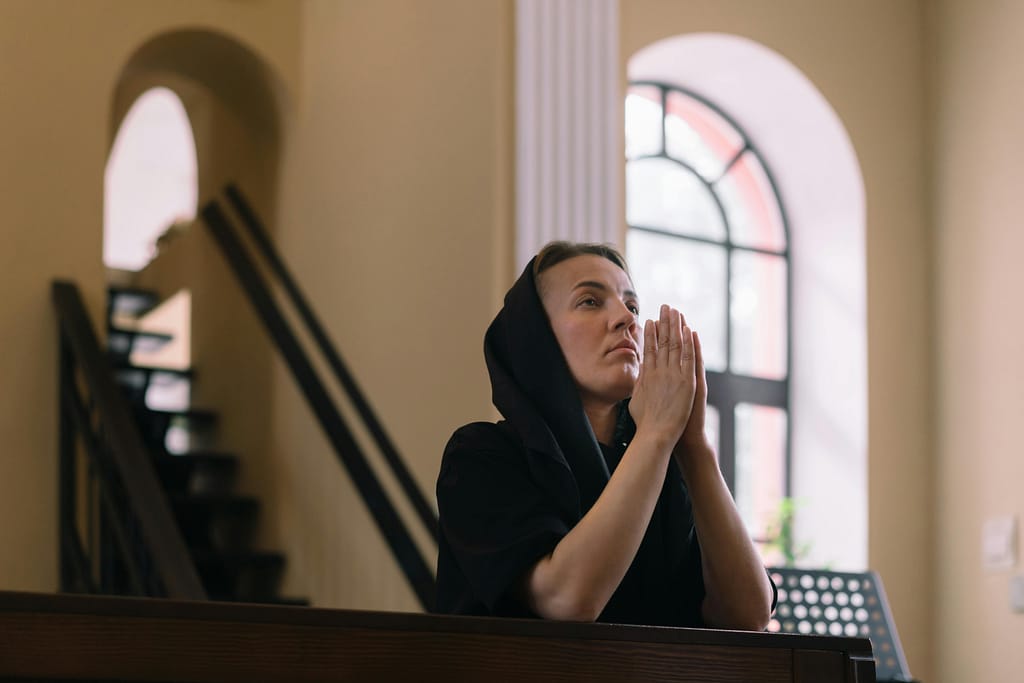 A Catholic woman in a headscarf prays inside a peaceful church, expressing devotion and spirituality.