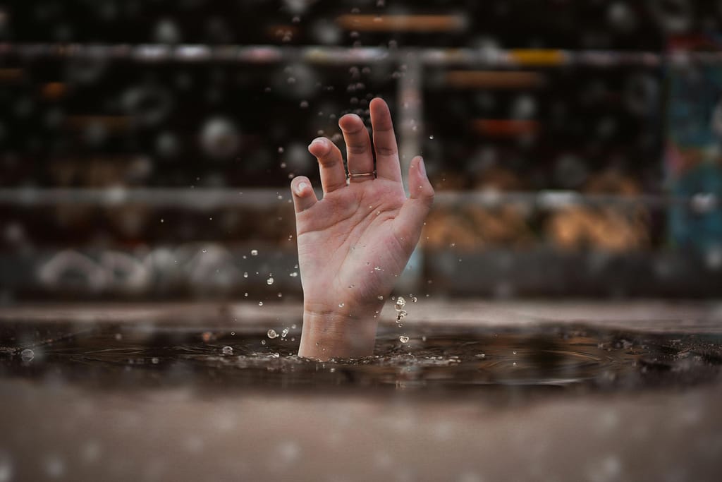 A single hand emerges from water, symbolizing a cry for help amidst a rainy setting.