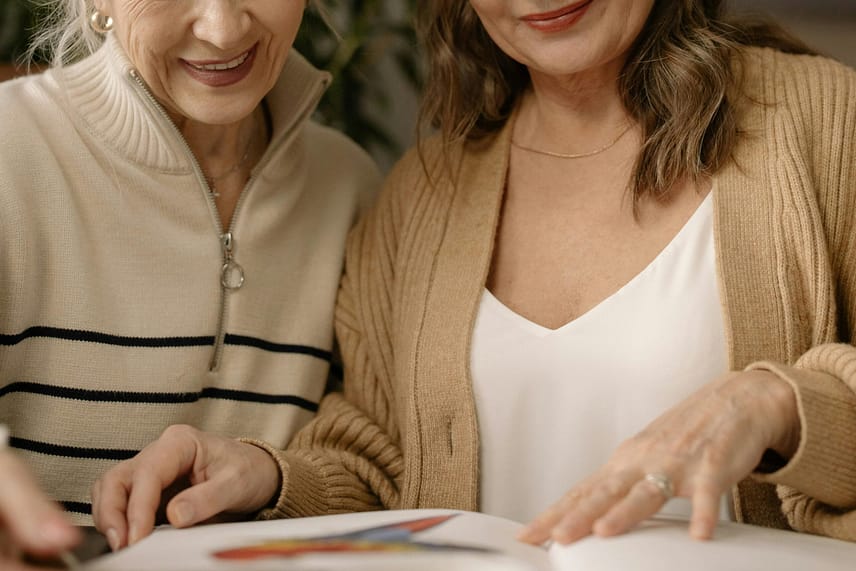 Two senior women enjoy reading a book together indoors, sharing smiles and companionship. Starting Over: The Brave, Beautiful Gift of God’s Grace