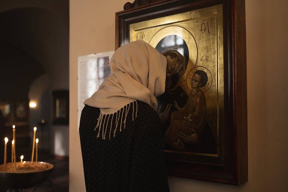 A woman with a headscarf prays before Mother Mary in a dimly lit church, creating a serene religious atmosphere.